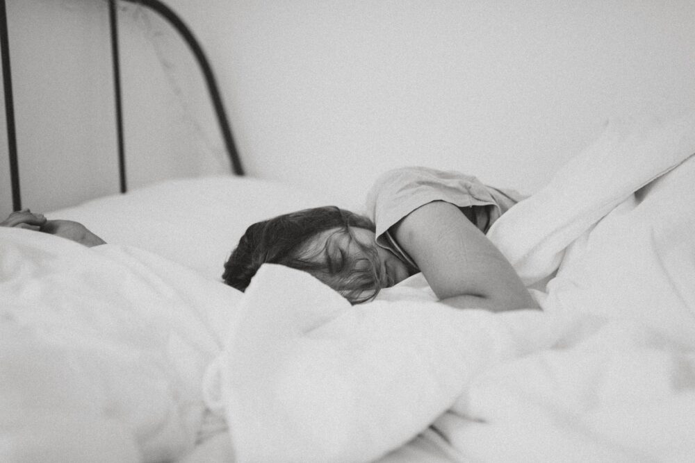 Night sweats - Black and white photo of a dark-haired woman sleeping in a bundle of white blankets in bed.