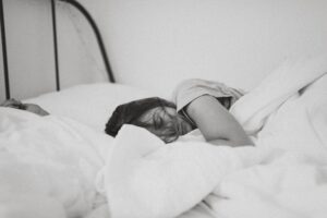 Night sweats - Black and white photo of a dark-haired woman sleeping in a bundle of white blankets in bed.